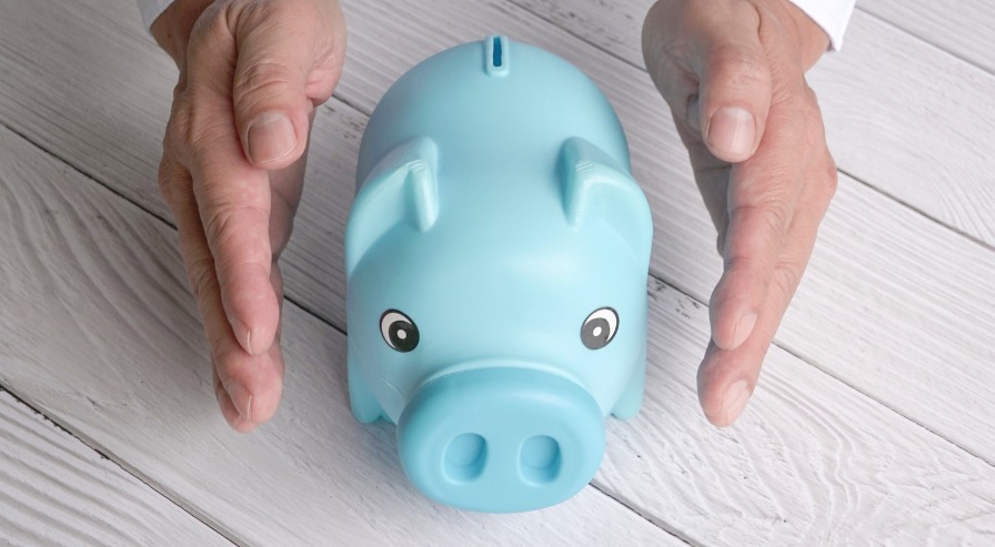 Hands protecting a blue piggy bank, symbolizing saving and safeguarding financial investments.