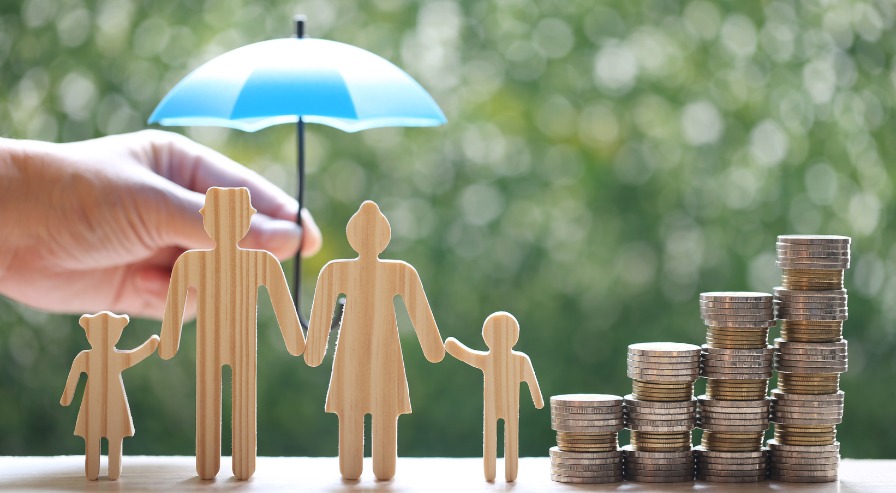 Wooden family figures sheltered by a blue umbrella beside stacked coins, illustrating strategic family investment planning and financial security