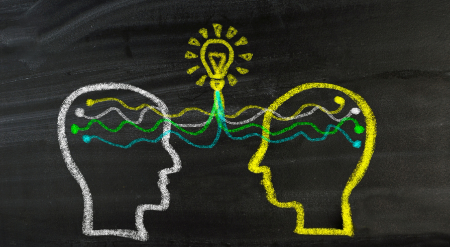 Chalk drawing of two heads connected by waves and a lightbulb, representing shared ideas and insights in psychology of investing.