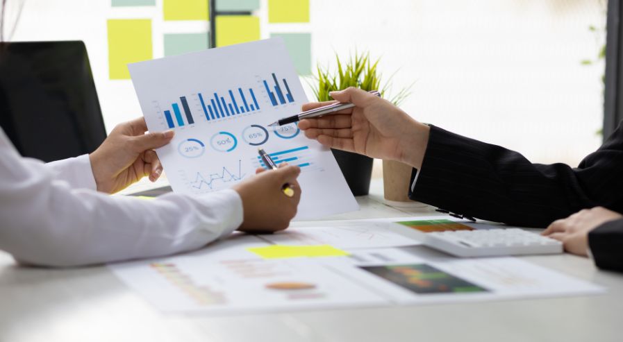 Two people analyzing charts and graphs during a business meeting, with a calculator and a small plant on the table.